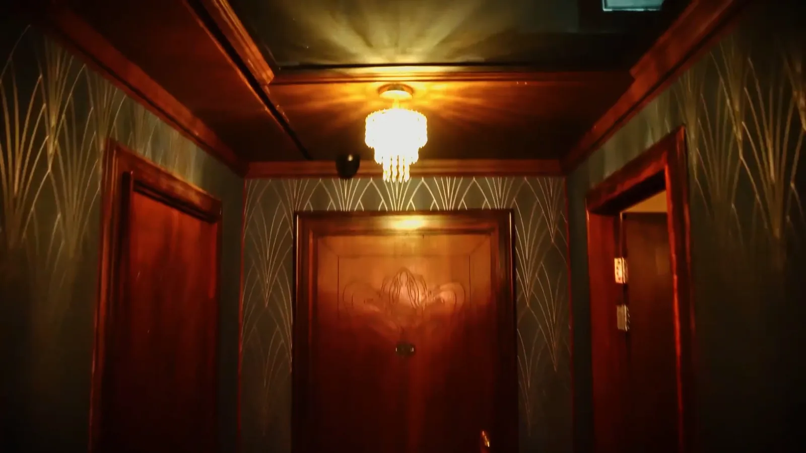 A timber-panelled hotel corridor in Hotel: Murder Mystery lit by a crystal chandelier