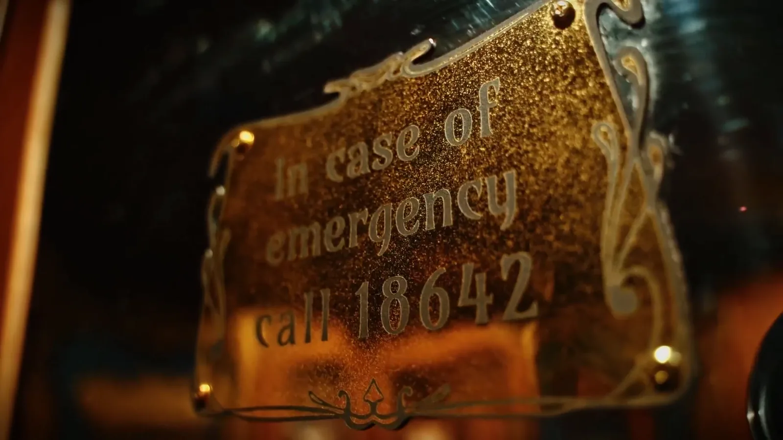 A gilded lift plaque reading In case of emergency call 18642 in Hotel: Murder Mystery
