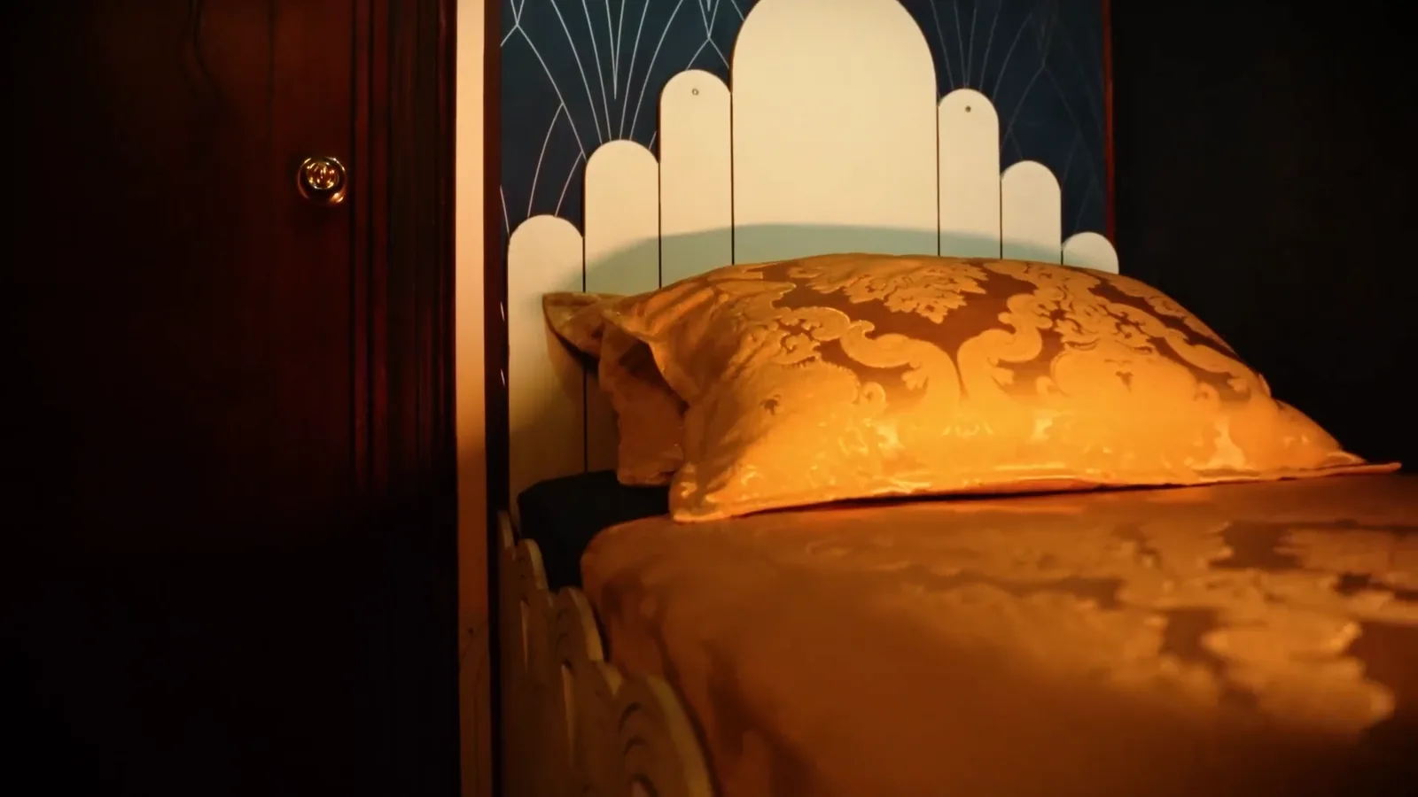 A gold damask bed with an Art Deco headboard in the Hotel: Murder Mystery suite
